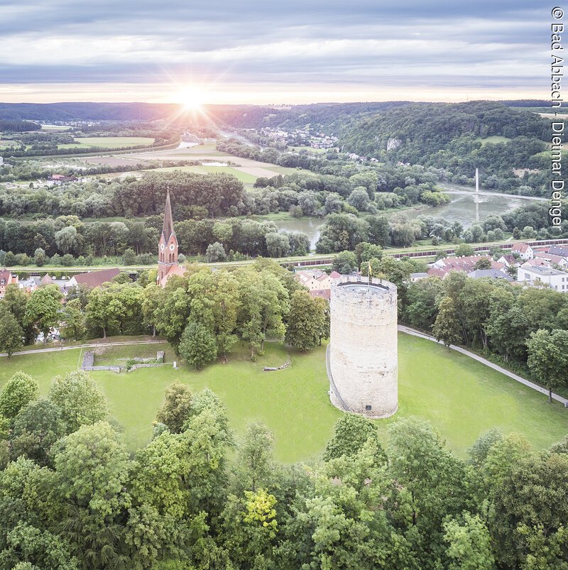 Bad Abbach Burgberg Vogelperspektive Luftaufnahme einer Landschaft mit einem runden Turm und einer Kirche mit spitzem Turm, umgeben von Bäumen und Wiesen.