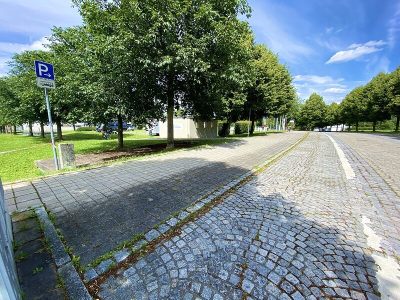 Parkplatz f&uuml;r Busse mit gepflasterter Fl&auml;che neben Baumreihe und blauem Himmel bei Tag