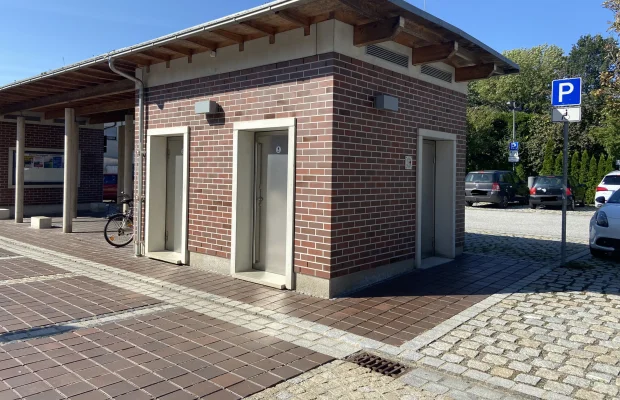 Gebäude mit drei Türen, Parkplatz mit Behindertenparkplatzschild und mehreren Autos im Hintergrund.