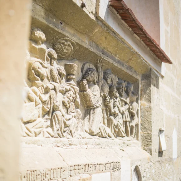 Steinrelief an einer Außenwand mit mehreren Figuren in historischer Kleidung, darunter eine betende Person.