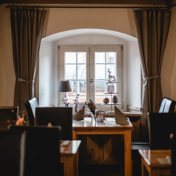 Essbereich mit Tisch und Stühlen vor einem Fenster mit Vorhängen, dekoriert mit Lampe und Figuren.