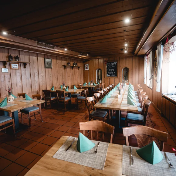 Holzgetäfelter Gastraum mit gedeckten Tischen, grünen Servietten und Stühlen, Fenster auf der rechten Seite.