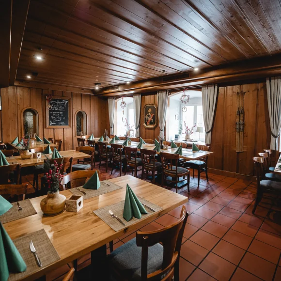 Holzvertäfelter Gastraum mit gedeckten Tischen, grünen Servietten und Dekorationen, Fenster mit Vorhängen im Hintergrund.